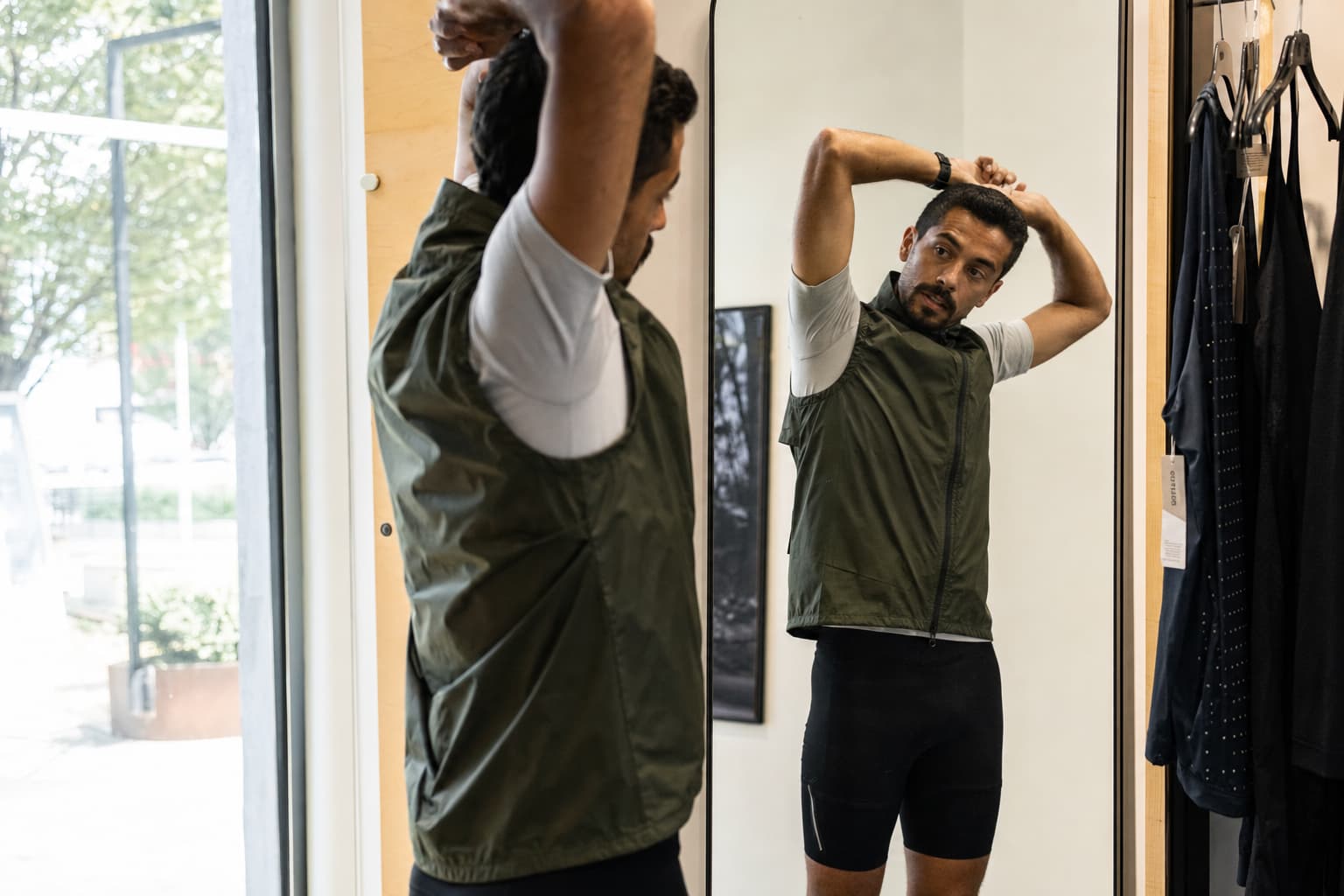 Un coureur essayant une veste de course sans manches, levant les bras et se tordant le torse, contrôlant sa mobilité dans le reflet d