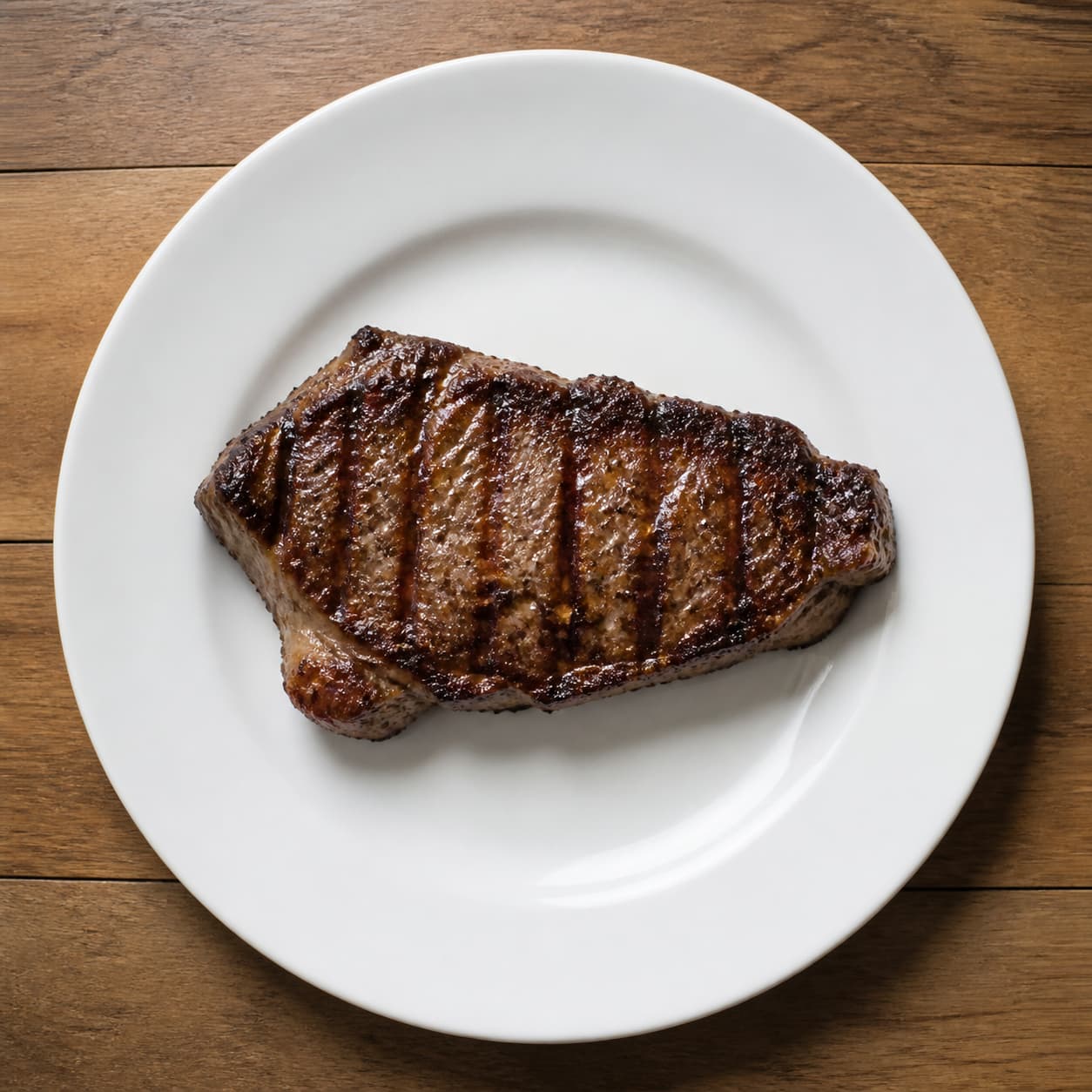 Assiette blanche avec un seul steak grillé, sans légumes ni féculents, posée sur une table en bois.